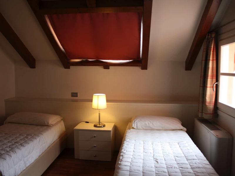 Een kamer met schuin plafond, twee eenpersoonsbedden en een nachtkastje met lamp ertussen.