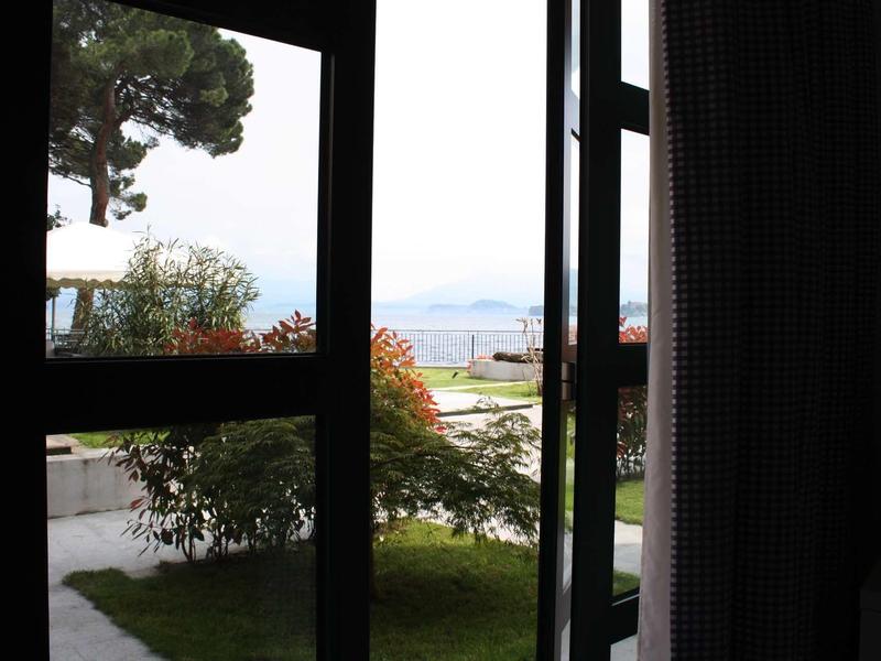 Uitzicht door een donker raam op een tuin met bomen en bergen op de achtergrond.