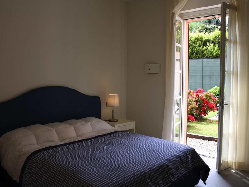 Slaapkamer met tweepersoonsbed, nachtlampje en deur naar bloeiende tuin.