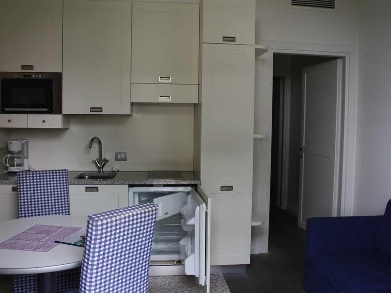 Kleine kitchenette met koelkast, magnetron, tafel en stoelen in een hotelkamer.