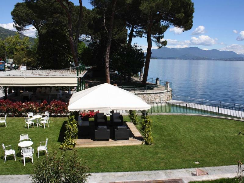 Groene tuin met witte stoelen en parasol naast een rustig meer onder een blauwe lucht.