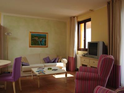 Gemütliches Wohnzimmer mit lila Stühlen, Sofa, TV und großen Fenstern mit Vorhängen.