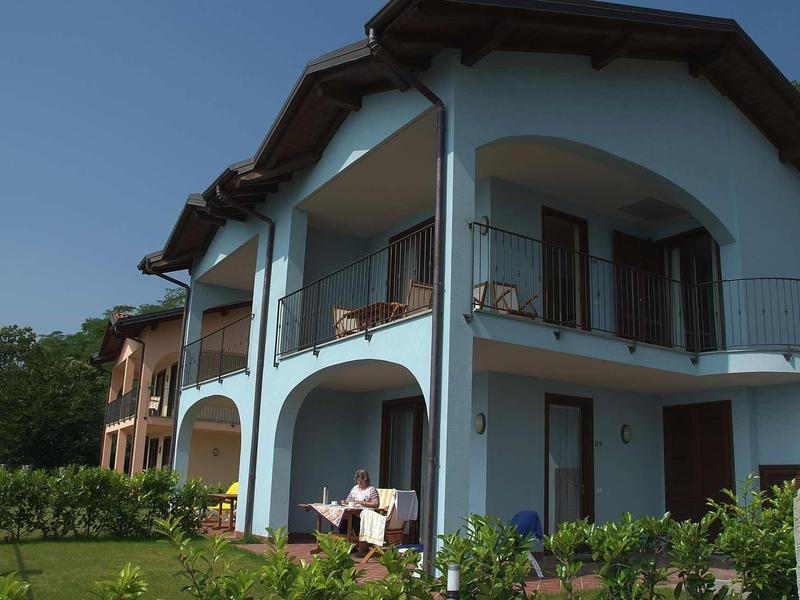 Zweistöckiges Haus mit blauer Fassade, Balkon, braunen Fensterläden und Garten im Vordergrund.