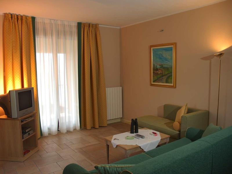 Gemütliches Wohnzimmer mit grünem Sofa, Sessel, Couchtisch, TV und gelben Vorhängen.