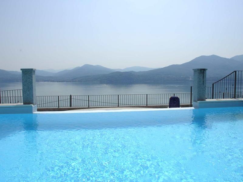 Blauer Pool mit klarem Wasser vor nebligen Bergen und ruhigem See im Hintergrund.