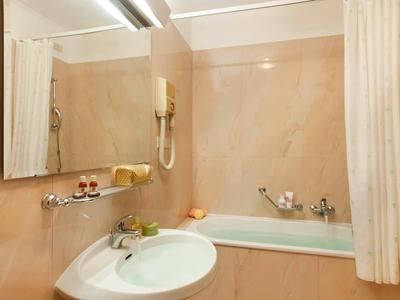 Kleines Badezimmer mit Waschbecken, Badewanne und Spiegel mit Haarföhn.