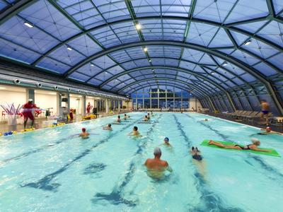Überdachtes Schwimmbad mit mehreren Personen beim Schwimmen und Entspannen im Wasser.