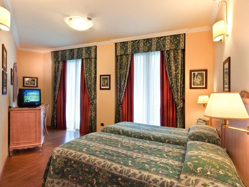 Cozy hotel room with two beds, TV, and decorative curtains on the windows.