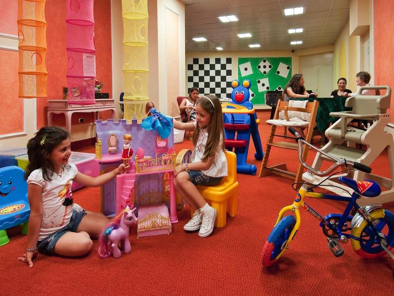 Children playing with toy horses in a colorful playroom with carpeted floor.