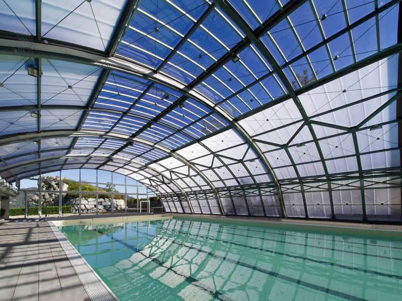 Indoor pool with glass roof and view of outdoor area under clear sky.