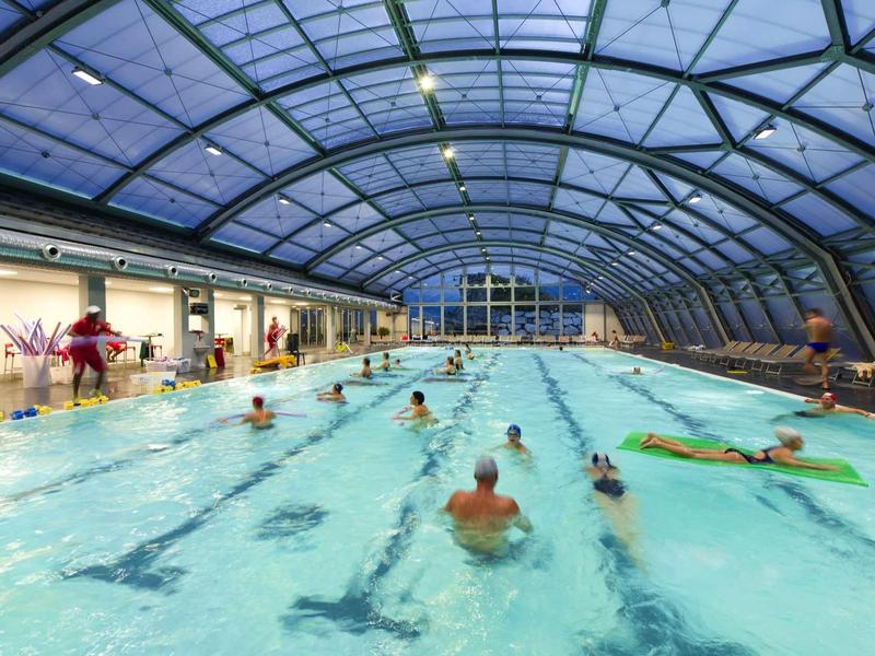 Indoor covered swimming pool with several swimmers and a glass roof.