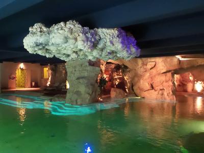 Beleuchteter Pool mit Felswand und künstlichem Baum unter blauem Himmel in einer Hotelanlage