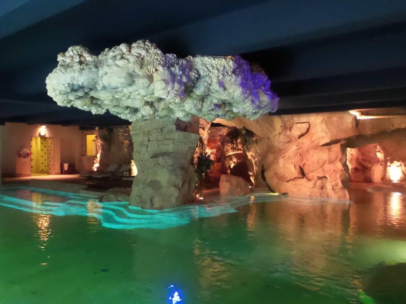 Piscine intérieure éclairée avec cascade et rochers dans un hôtel