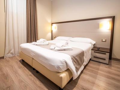 Modernes Schlafzimmer mit großem Doppelbett, weiße Bettwäsche, Nachttisch und warmen Lichtquellen.