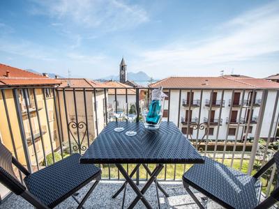 Balkon mit schwarzem Tisch und Stühlen, blauer Getränkekaraffe, Blick auf Häuser und Berge im Hintergrund.