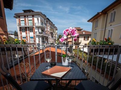 Balkon mit Tisch, zwei Weingläsern und Blumen, umgeben von Wohngebäuden unter blauem Himmel.