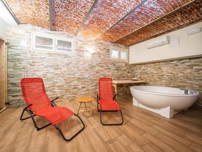 Kellerraum mit roten Liegestühlen, freistehender Badewanne und Steinwand, Holzoptikboden und Ziegeldecke.