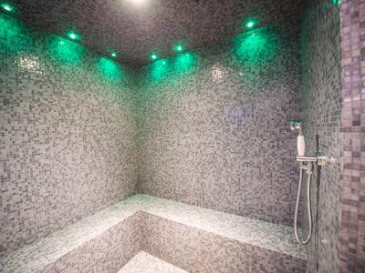 Moderner Mosaik-Duschbereich mit integrierter Bank und grüner LED-Beleuchtung an der Decke.