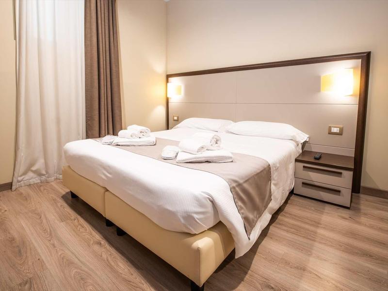 Modernes Schlafzimmer mit großem Doppelbett, weiße Bettwäsche, Nachttisch und warmen Lichtquellen.