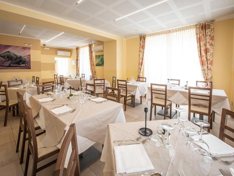 Ein heller Speisesaal mit gedeckten weißen Tischen und Holzmöbeln, große Fenster mit Gardinen.