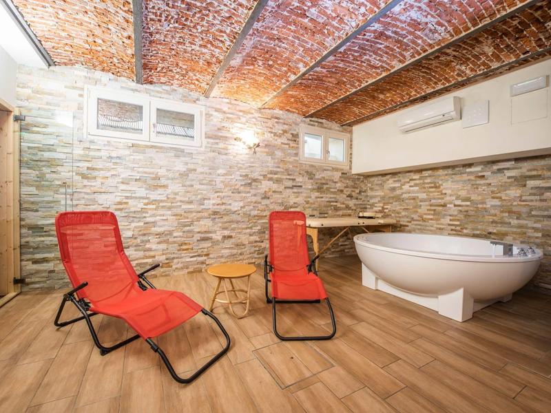 Kellerraum mit roten Liegestühlen, freistehender Badewanne und Steinwand, Holzoptikboden und Ziegeldecke.