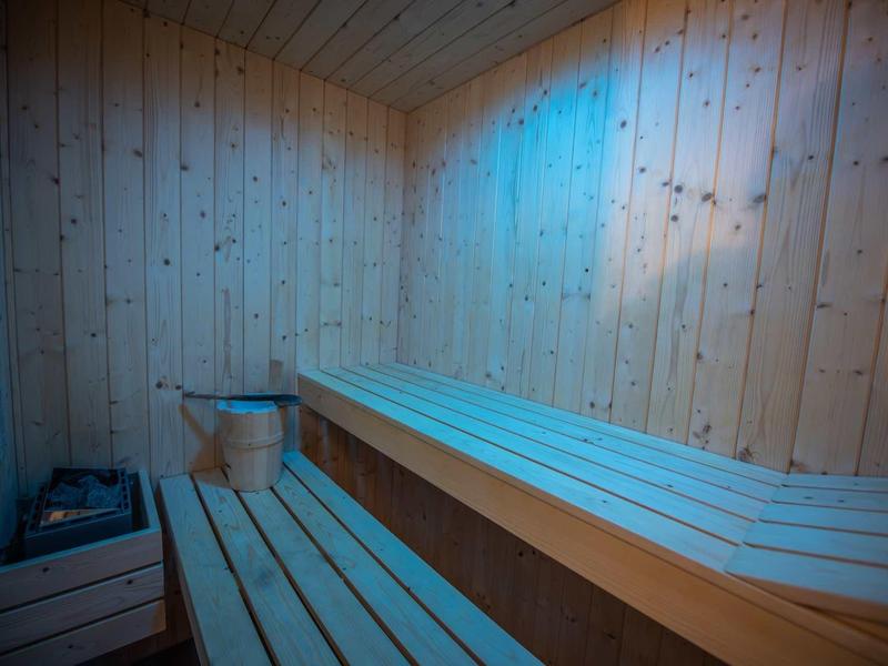 Sauna mit hellen Holzbänken und Wänden, Eimer und Kelle, blaues Licht an der Decke.