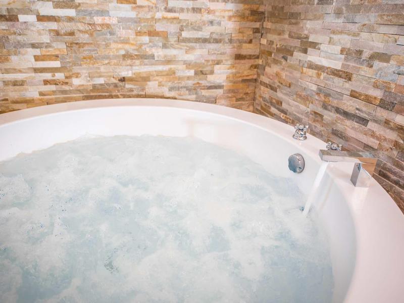 Rundes Whirlpool mit sprudelndem Wasser vor einer Wand mit braunen Natursteinfliesen.