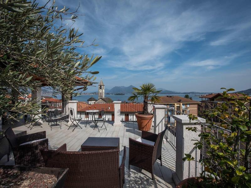 Terrasse mit Holzmöbeln, Pflanzen und Blick auf rote Dächer unter bewölktem Himmel.
