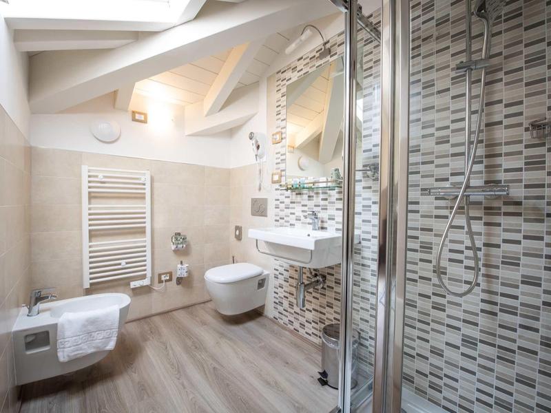 Modernes Badezimmer mit Dusche, Wand-WC, Handtuchheizung und großem Spiegel unter Dachschräge.