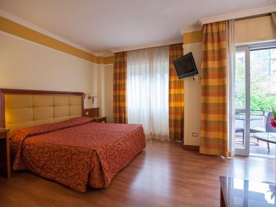 Gemütliches Schlafzimmer mit großem Bett, Holzfußboden, Vorhängen und Fernseher an der Wand.