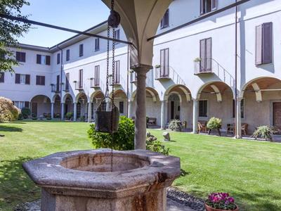 Innenhof mit grünem Rasen, altem Steinbrunnen und einem Gebäude mit Rundbogenarkaden.