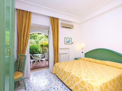 Hell eingerichtetes Hotelzimmer mit gelbem Bett und Balkon mit Gartenblick.