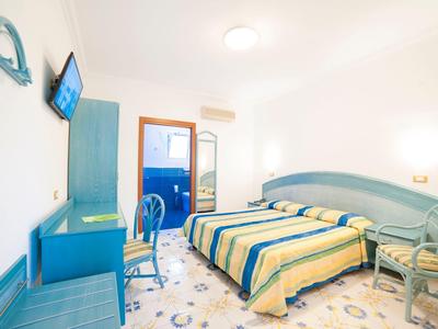 Helles Schlafzimmer mit zwei Einzelbetten, blau-gelben Bettdecken, Schreibtisch und Balkon.