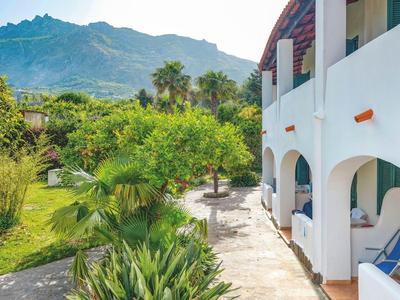 Weißes Hotelgebäude mit Balkon und Garten mit Bergen im Hintergrund