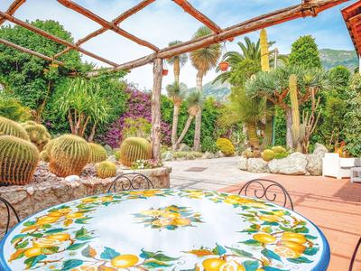 Bunte Mosaiktisch auf Terrasse mit Kakteen und Palmen im sonnigen Garten.