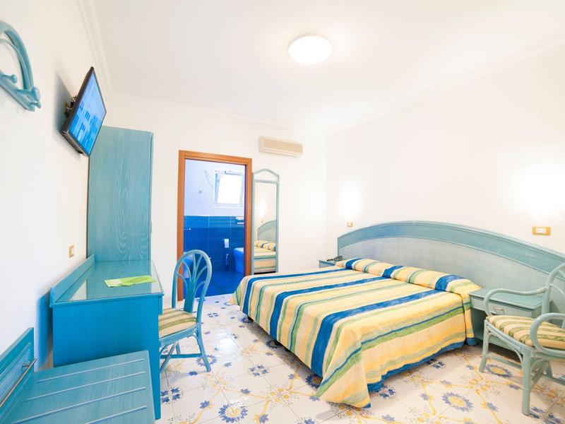 Helles Schlafzimmer mit zwei Einzelbetten, blau-gelben Bettdecken, Schreibtisch und Balkon.