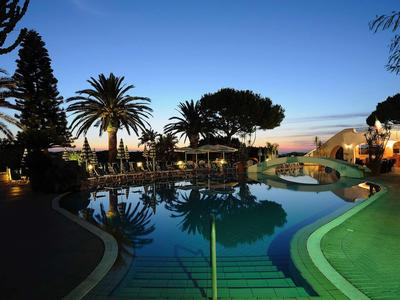 Beleuchteter Hotelpool bei Sonnenuntergang mit Palmen und Sitzbereichen im Freien.