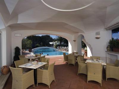 Überdachte Terrasse mit hellen Rattanstühlen, Tischen und Blick auf einen Pool und Garten.