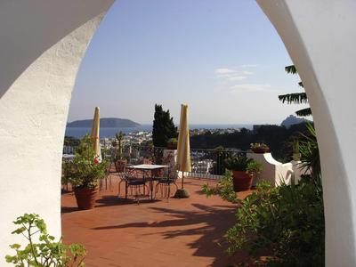 Terrazza con tavoli, sedie e ombrelloni con vista sulla città e sul mare.