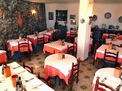 Ristorante accogliente con tovaglie rosse e bianche e parete in pietra rustica.
