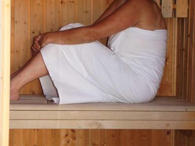 Frau in einem weißen Handtuch sitzt entspannt in einer Sauna aus Holz.