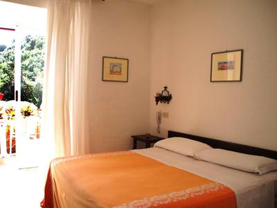 Camera d'hotel luminosa con letto matrimoniale, copriletto arancione e accesso a un balcone con piante.