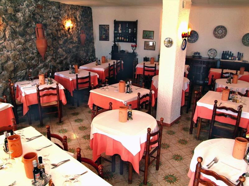Ristorante accogliente con tovaglie rosse e bianche e parete in pietra rustica.