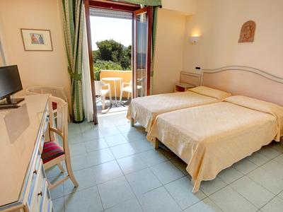 Bright hotel room with two single beds and balcony with green view.