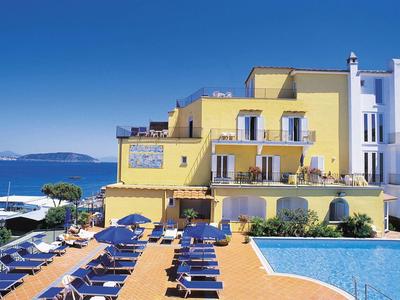 Hotel with yellow building, pool, and sun loungers by the sunny coastal beach