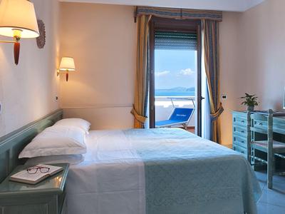 Bright hotel room with two beds, balcony overlooking the sea, and modern furnishings.