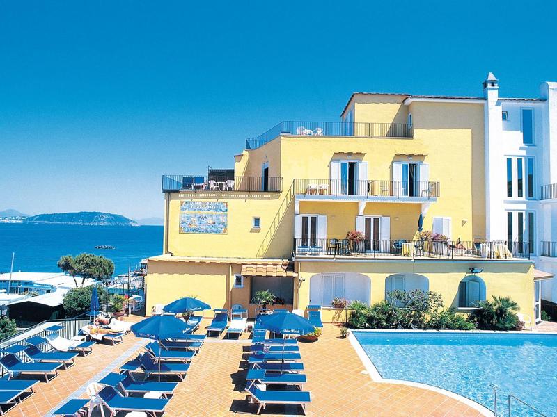 Yellow hotel with pool and sunbeds under clear blue sky by the sea
