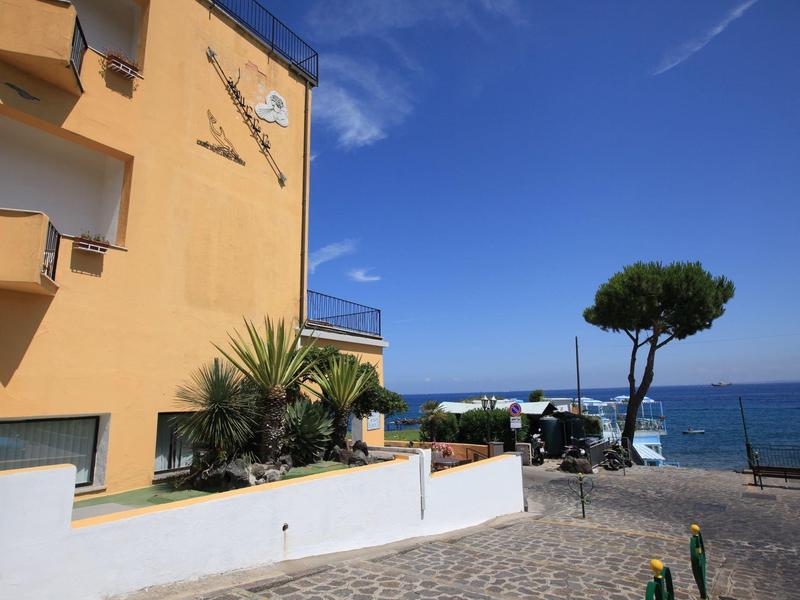Yellow building with balcony beside a paved path leading to the sea under clear sky.
