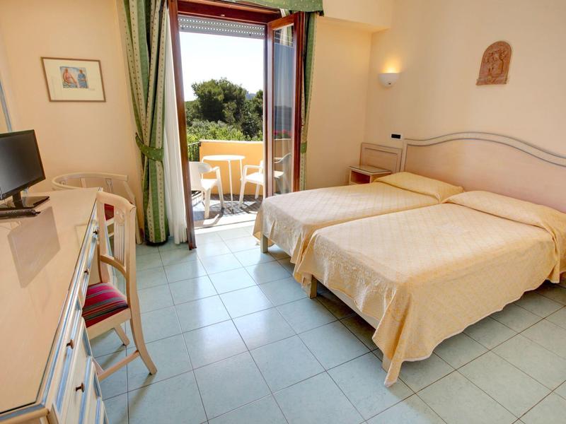 Bright hotel room with two single beds and balcony with green view.