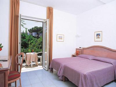 Chambre d'hôtel lumineuse avec deux lits et balcon donnant sur un feuillage vert